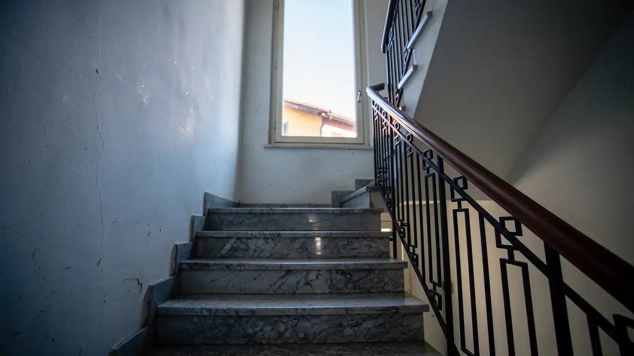 Scala di un condominio con gradini in marmo appena lavati, ringhiera in ferro e una finestra sul pianerottolo